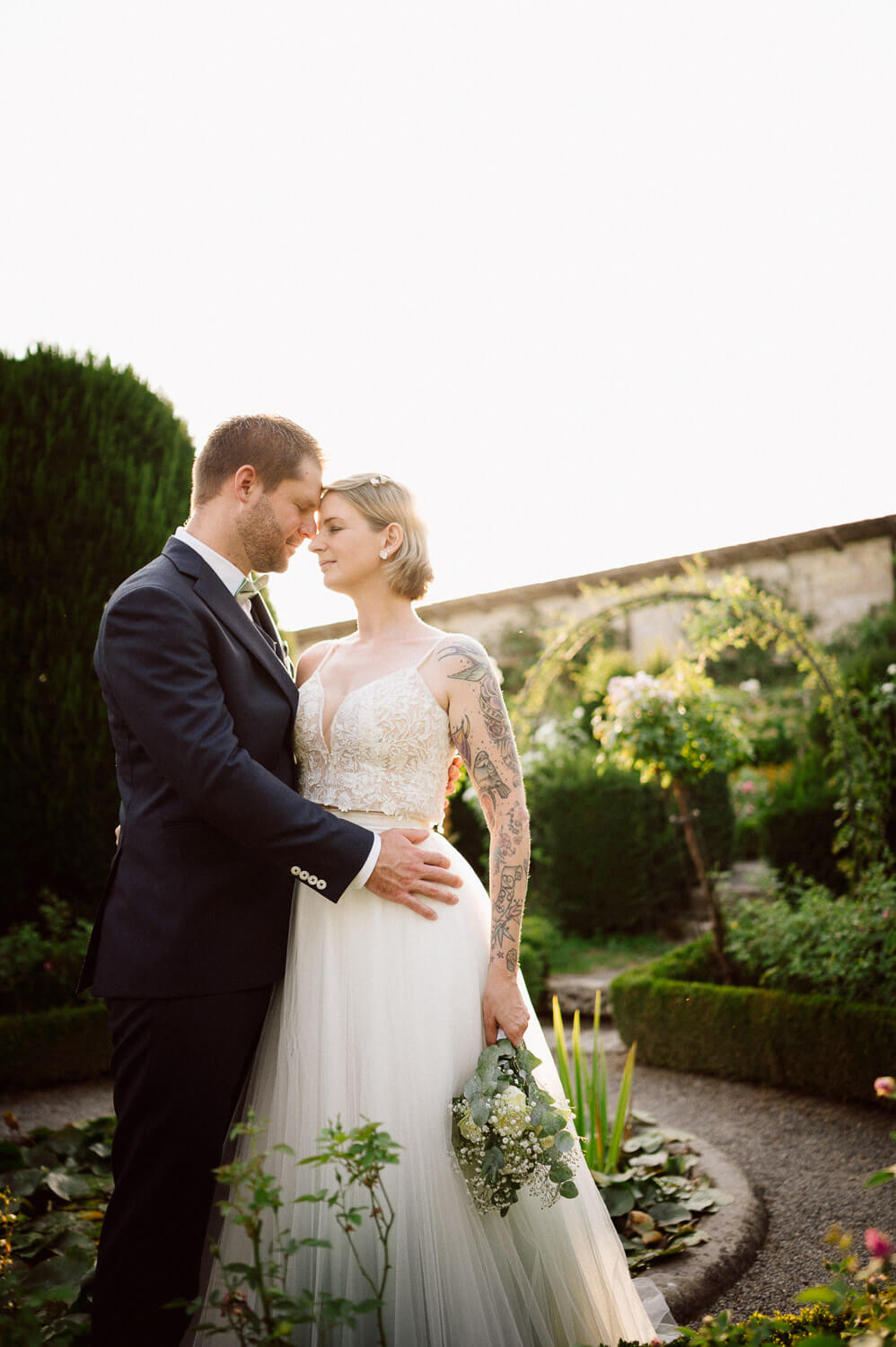 Bride and groom standing forehead to forehead in golden garden light.