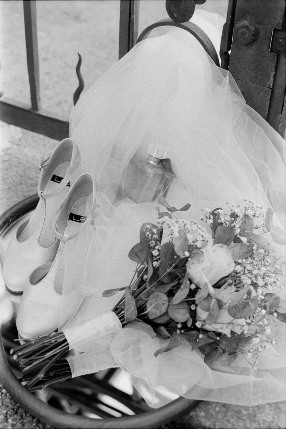 Black and white still life of bridal shoes, bouquet, and veil arranged together, luxury wedding photography.