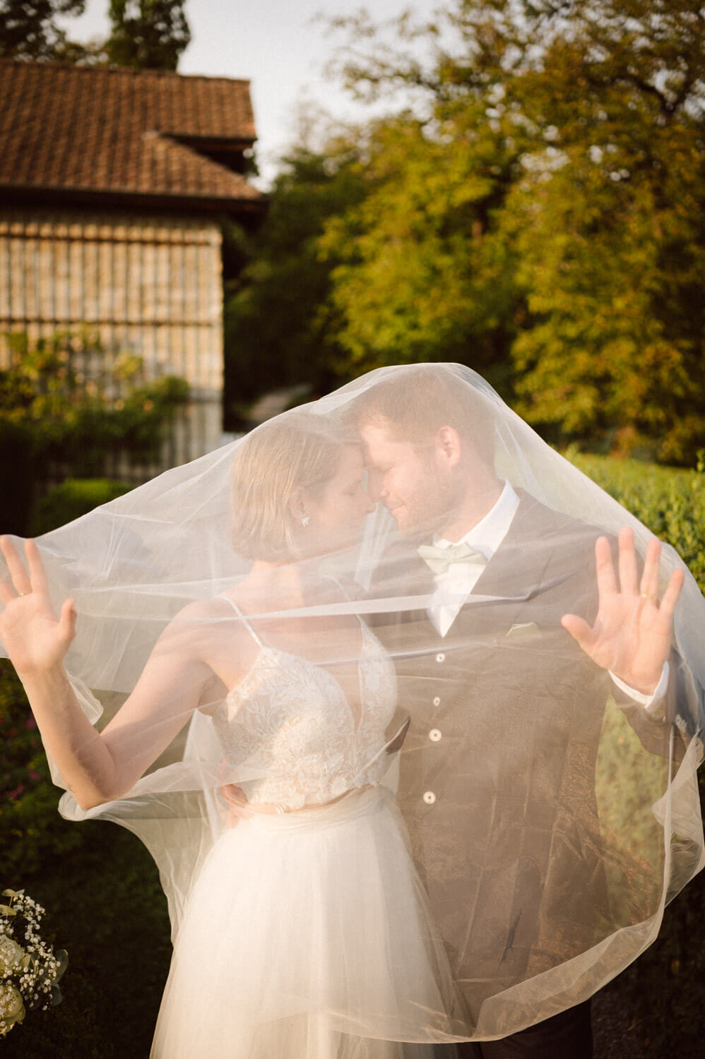 Bride and groom standing close together under a flowing wedding veil, luxury wedding photography.