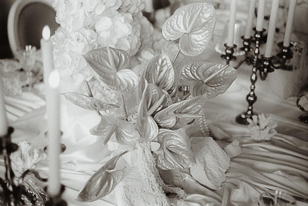 Black-and-white film shot of a pearlized anthurium centerpiece with candles on a draped reception table.