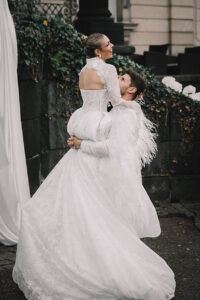 Groom lifts a laughing bride near ivy-covered terrace; sweeping train.