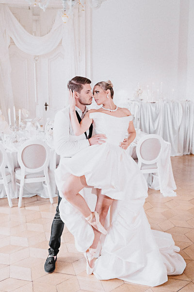 Swiss luxury wedding — editorial ballroom pose with the bride en pointe among all-white reception decor; digital.