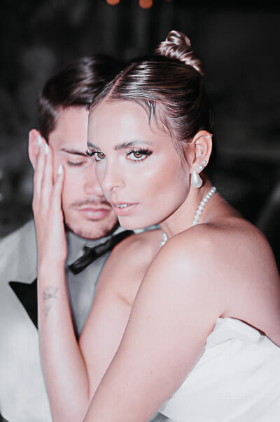 Swiss luxury wedding — cinematic close-up of the bride with pearl earrings and necklace, groom softly blurred; digital.