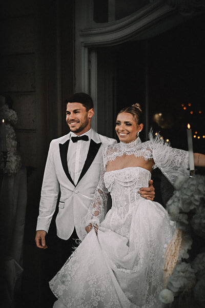 Swiss luxury wedding — smiling couple in a candlelit doorway framed by white florals; digital.