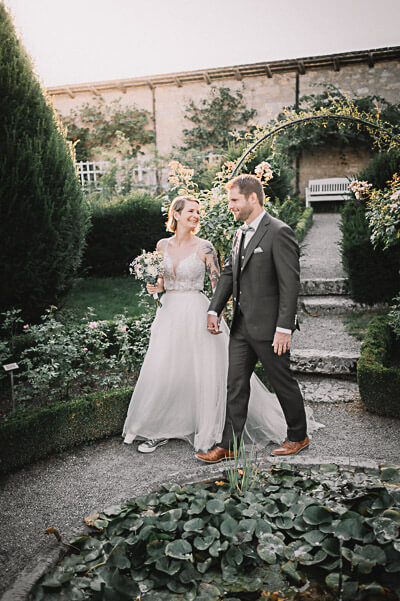 luxury wedding — couple walking through a formal garden under a floral arch; digital.