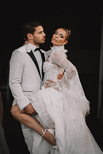Swiss luxury wedding — groom carrying the bride in a lace gown against a moody night backdrop; digital.