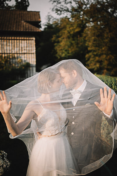 luxury wedding — bride and groom embracing under a veil at golden hour; digital.