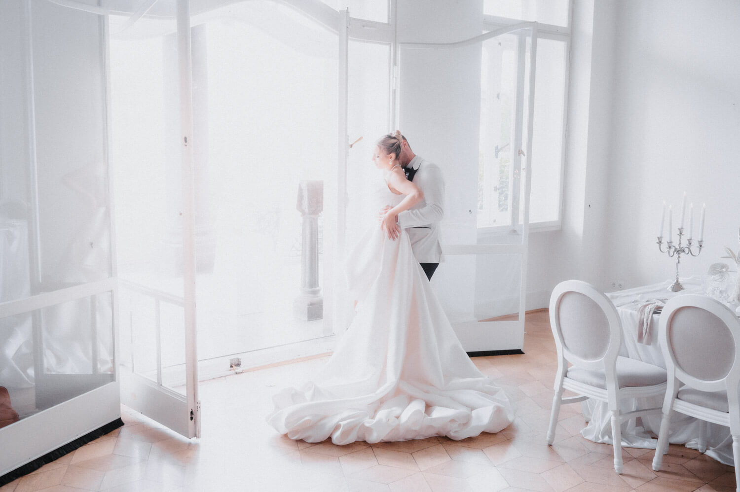 Brautpaar am Fenster mit fliessendem Kleid — natürliches Licht, Schweiz.