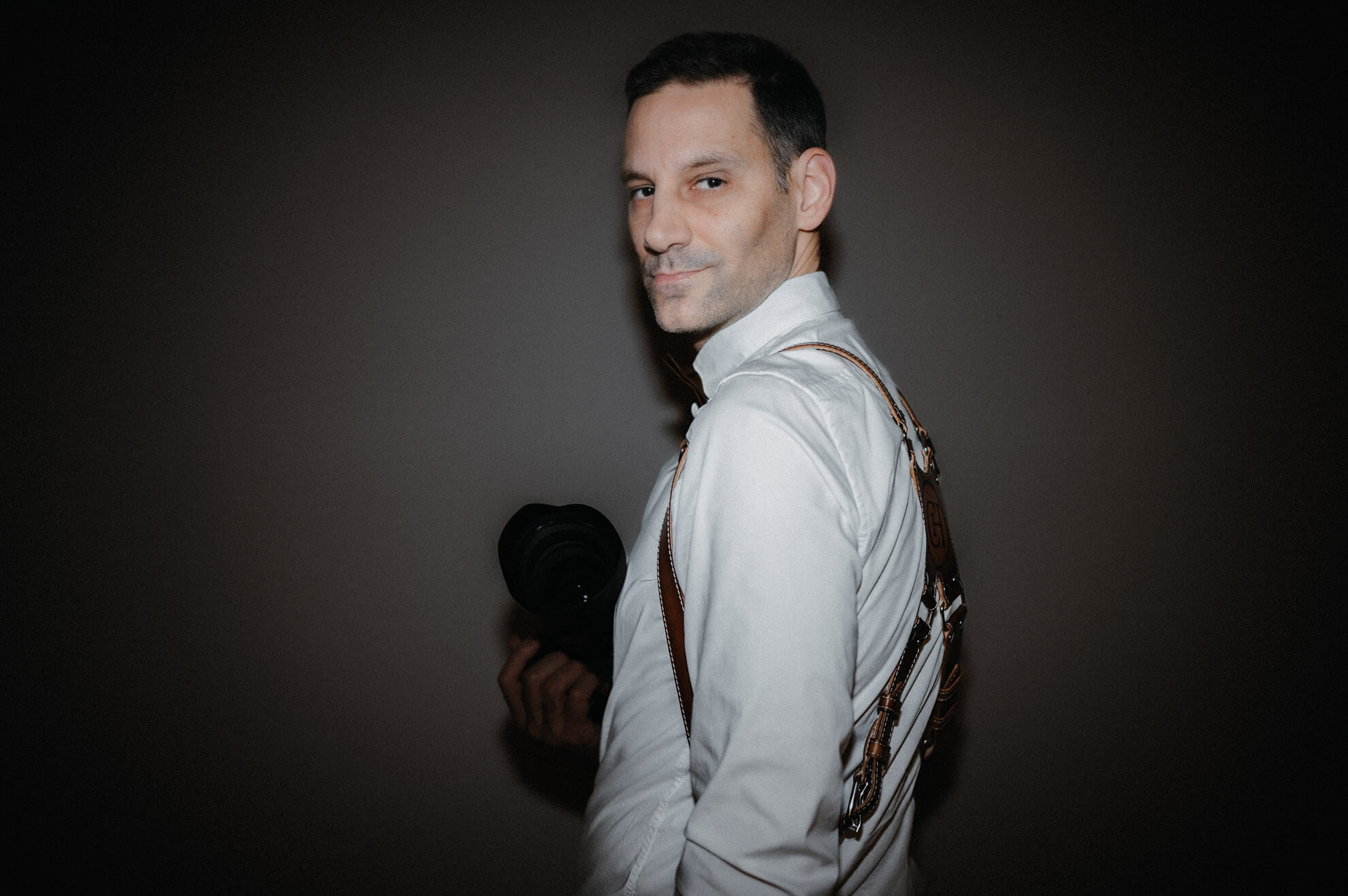 David Rickenbach, Swiss wedding photographer, portrayed in a calm editorial portrait holding a camera, representing timeless and emotional wedding photography.